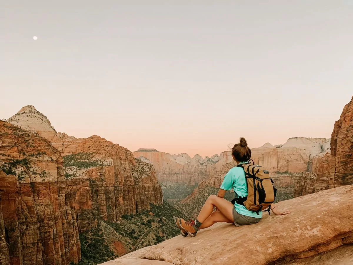 Woman hiker sitting on a red rock formation wearing a teal hiking tshirt.