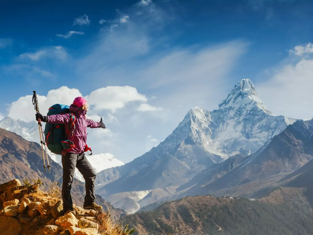 Women with a backpack stands in front of mountain backdrop on the Everest Base Camp trek.