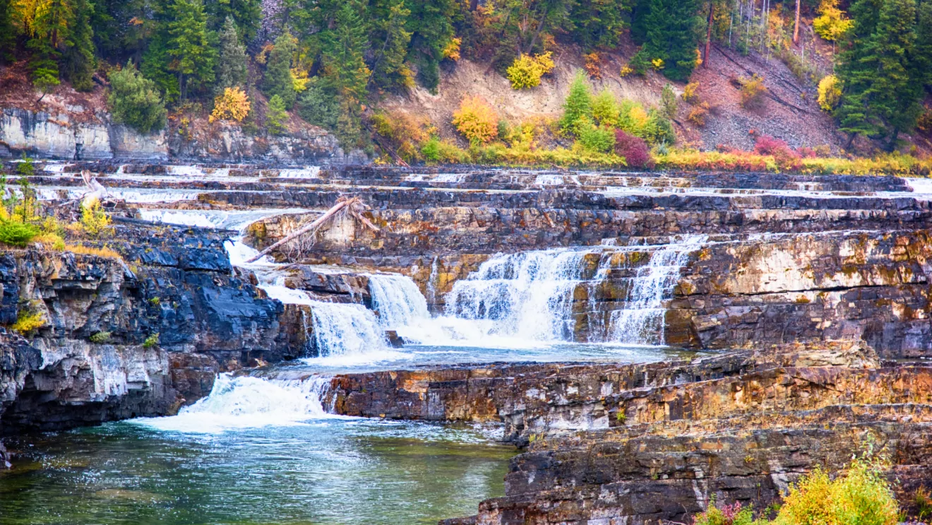 Bright fall colors surround a many streamed waterfall in the Kootenai Falls area of Montana