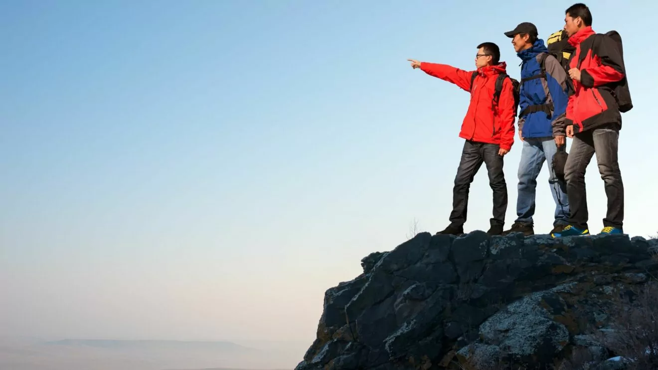 Three hikers pointing from the summit