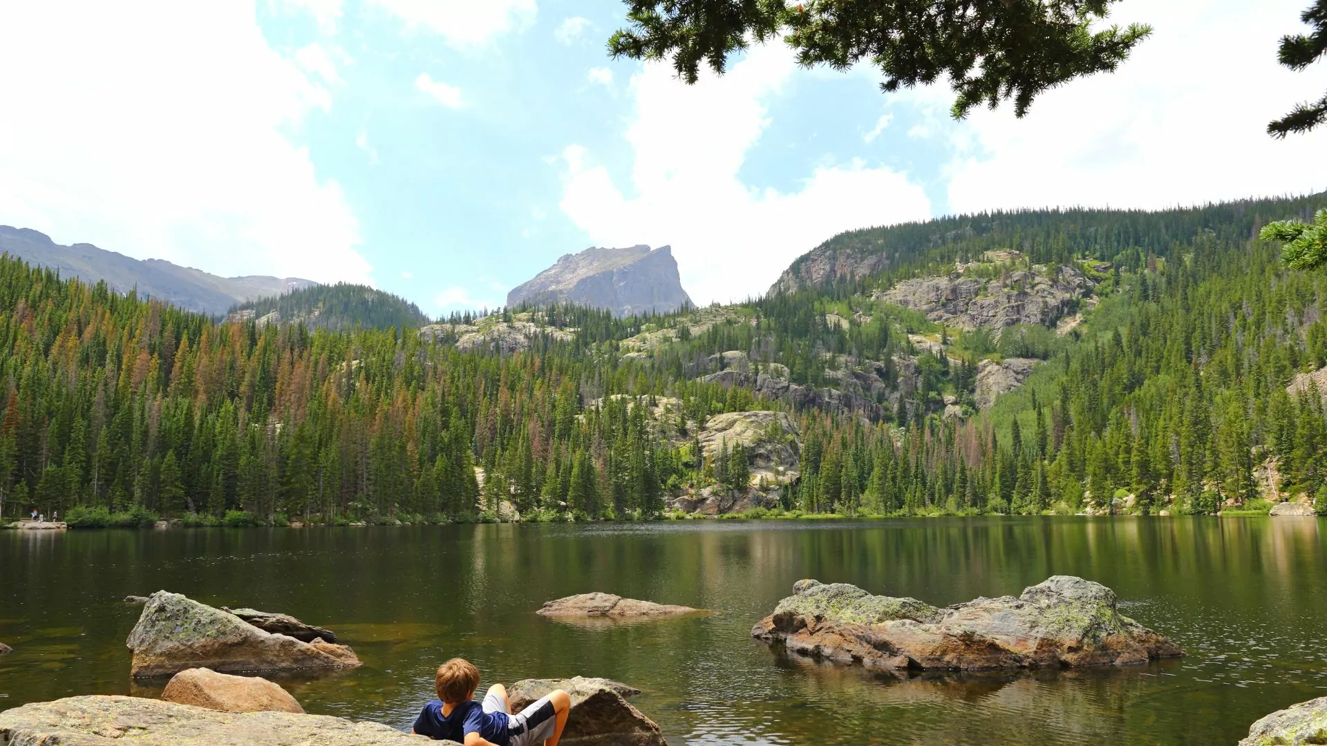 Someone reclines on a rock at the edge of a clear, still lake in the mountains
