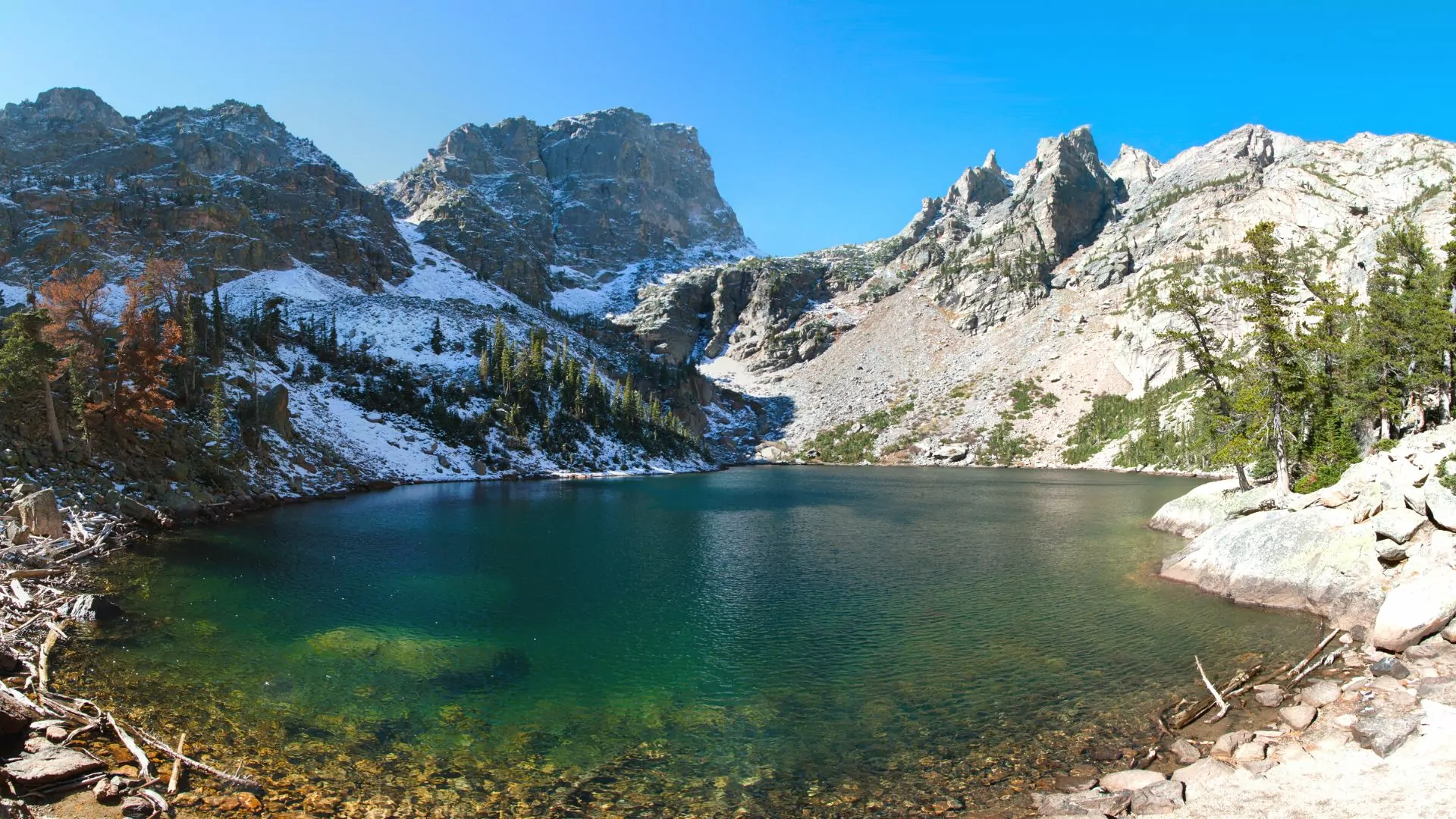 Deep green colored clear lake occupies lower half of photo with towering snowy peaks behind