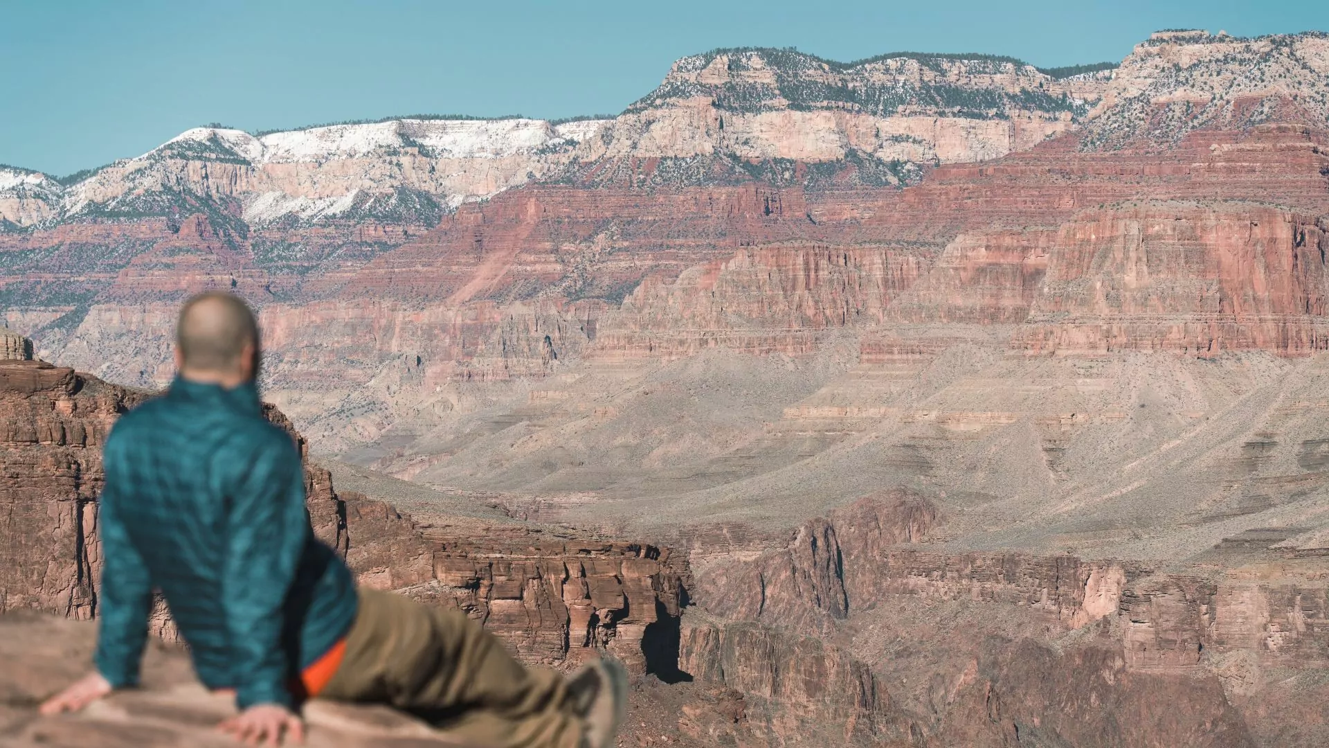 A man sits leaning back with legs outstretched taking in a view of the Grand Canyon
