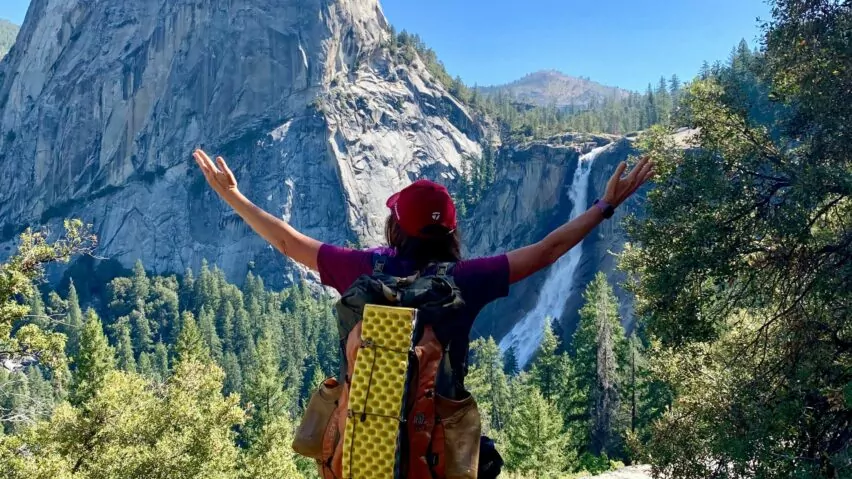 A backpacker celebrates in front of Nevada Falls after hiking the John Muir Trail