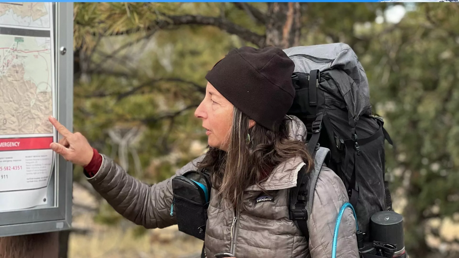 Wildland trekking guide with a backpack on points to a sign