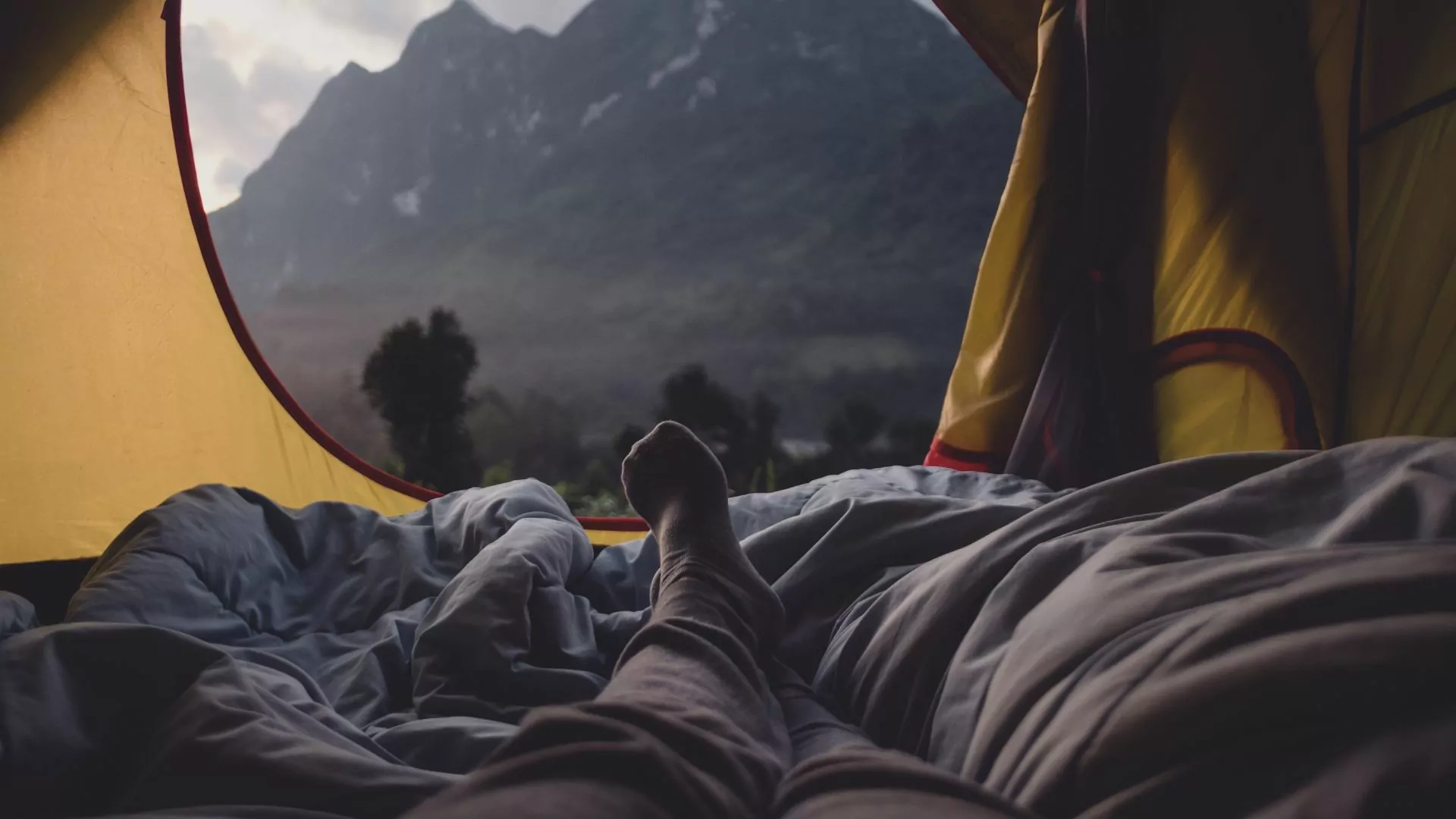 A tent doorway stands open with a nest of blankets inside and mountains rising in the distance