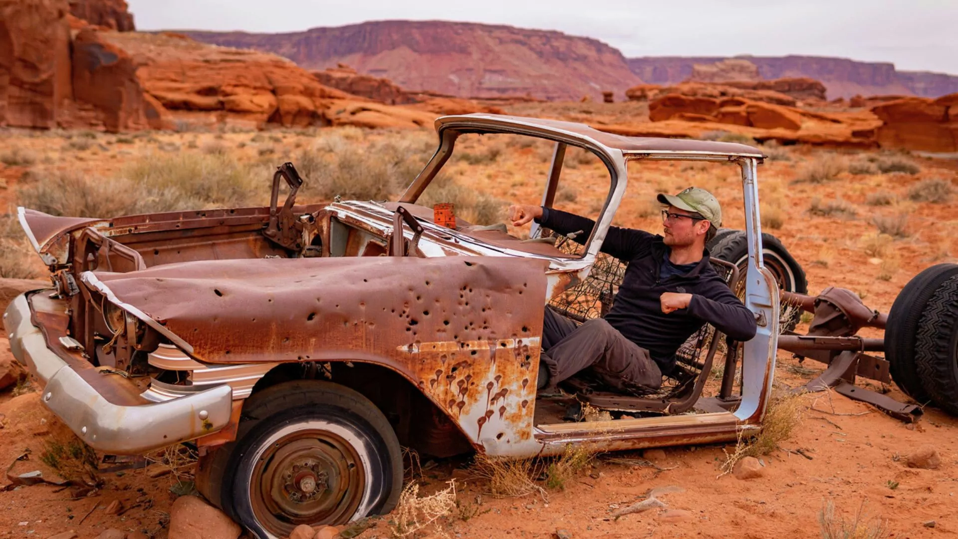 Guide and blog author Austin B. sits in an old broke down car in the desert pretending to drive