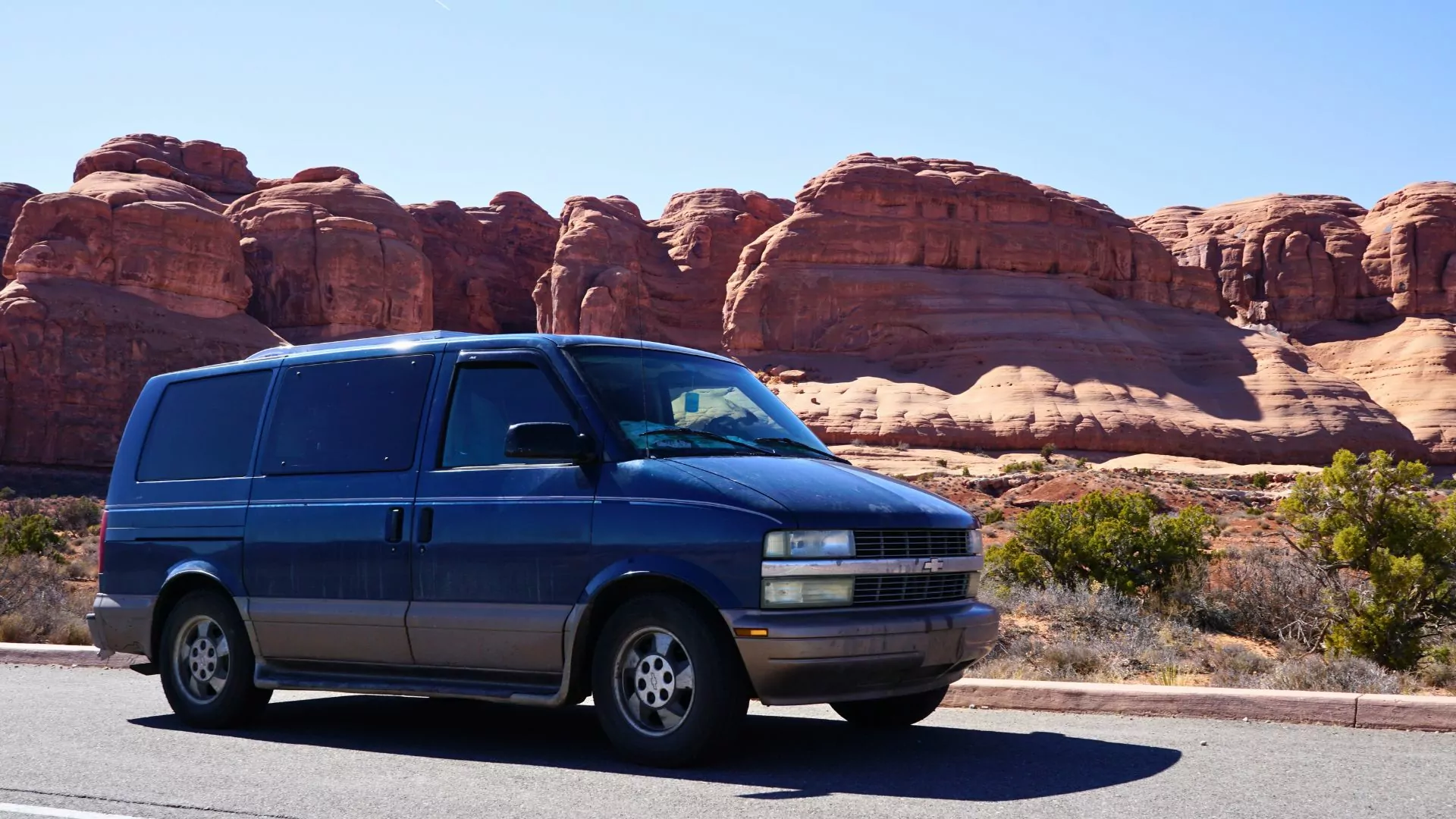 A Chevy Astrovan drives by red rock formations in the Utah desert