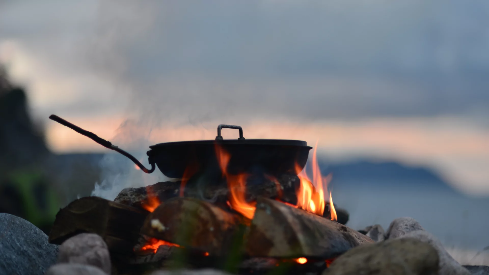 A frying pan simmers on a campfire at dusk