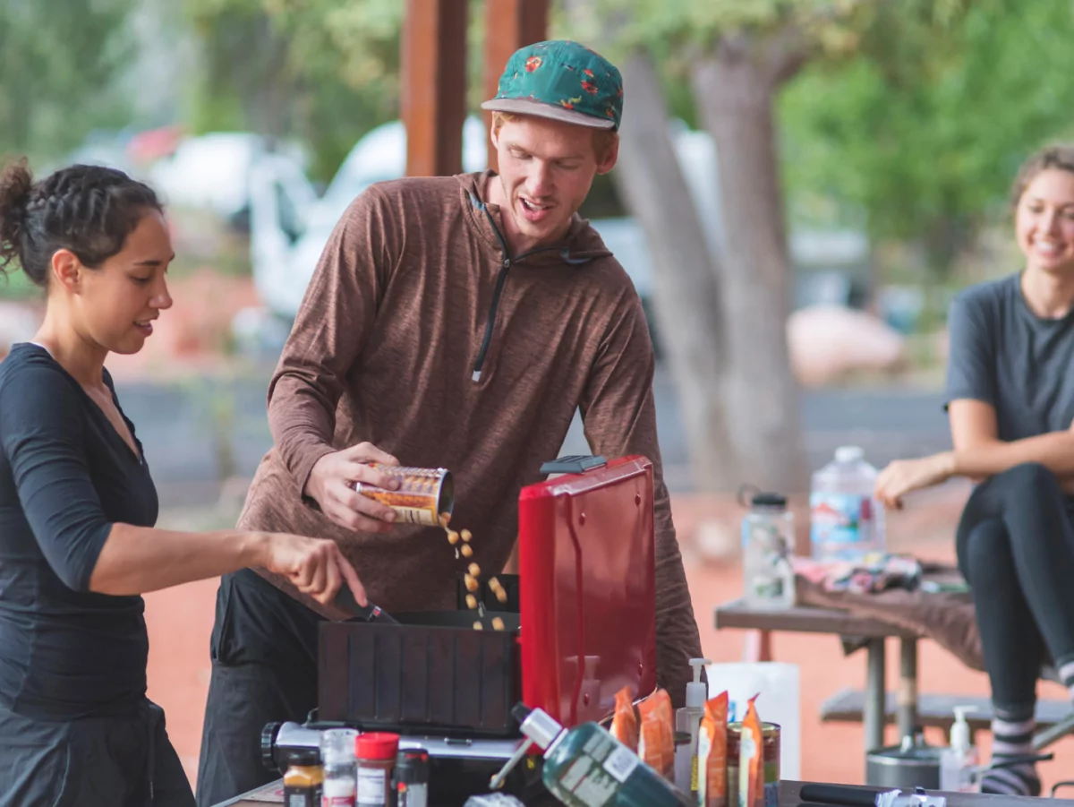 Friends cook a vegan meal outside on a camp stove