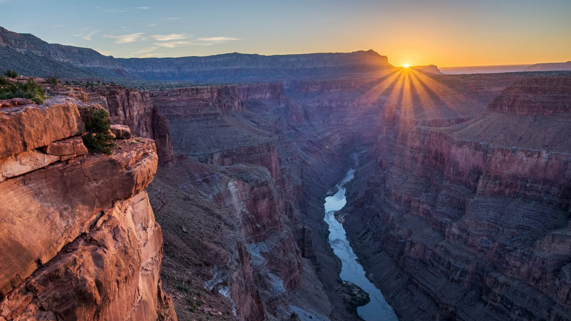 The rising sun sends rays of light shining over the south rim of the Grand Canyon as the Colorado River lies in shadow below