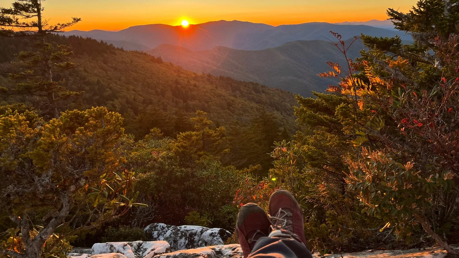 The crossed legs of a seated hiker look out over the sunset in the Shining Rock Wilderness