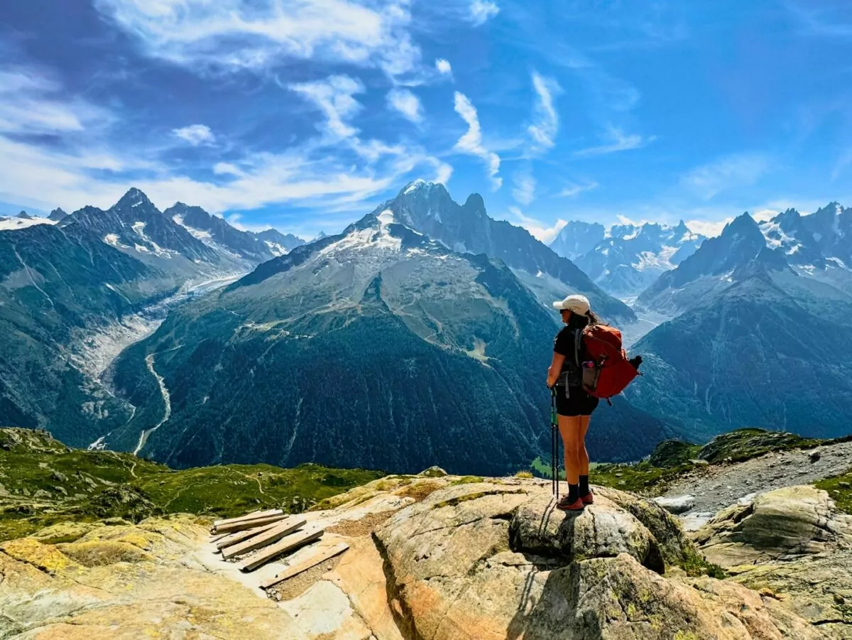 A woman poses in a daypack on a mountain top on the Tour du Mont Blanc