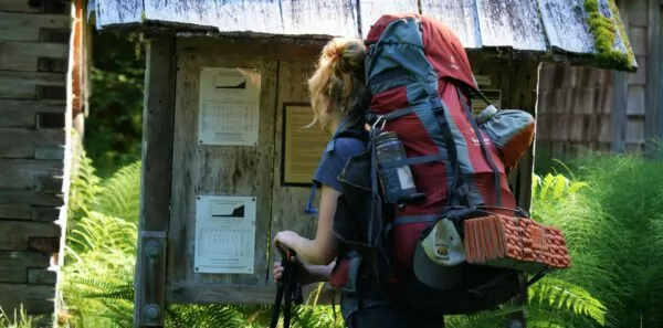 A woman with a backpacking pack on looks at a trailhead sign in the hoh rainforest