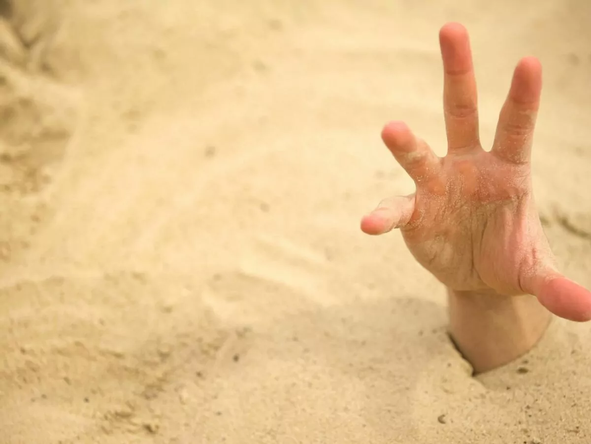 A hand reaches out of the sand