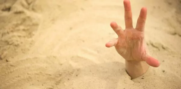A hand reaches out of the sand