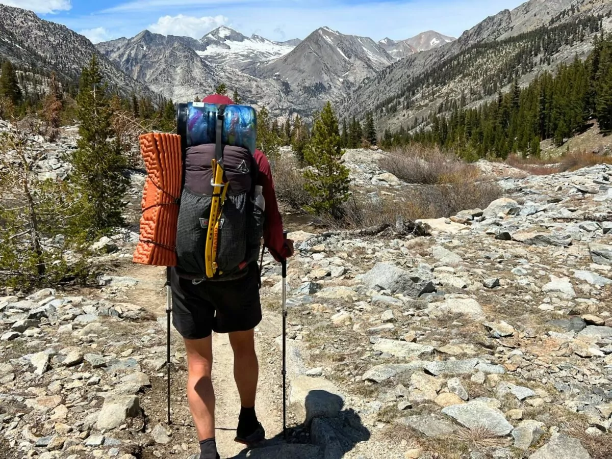 A thru hiker with a hyperlite backpack on follows a trail through the mountains