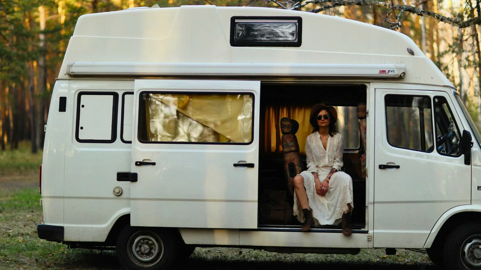 A woman sits in a camper van parked in the woods