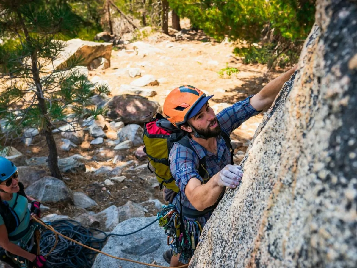 A man climbs granite with chalky fingers while a woman belays
