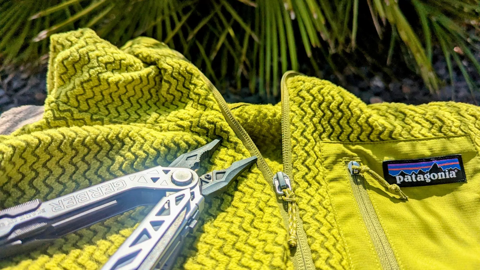 A pair of needle nosed pliers lay next to the zipper on a polar fleece