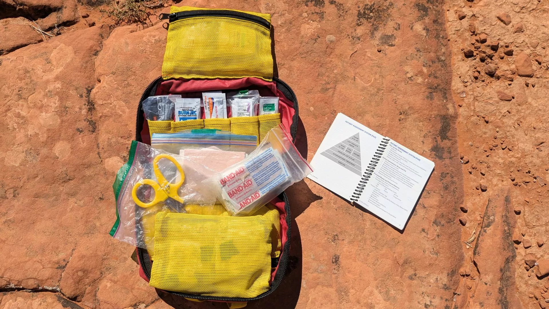 A booklet displays the patient assessment steps next to a first aid kit