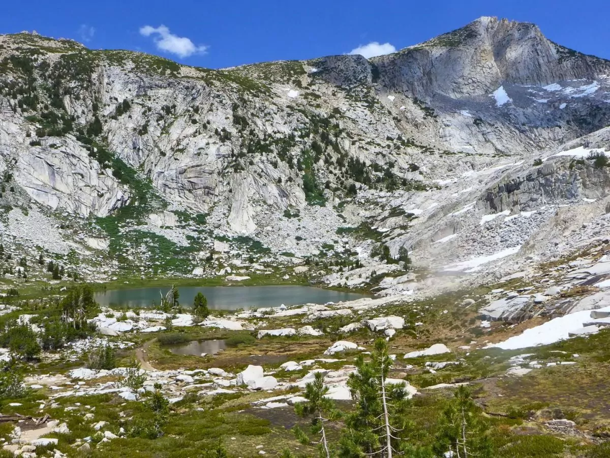 Ansel Adams wilderness in California's Sierra Nevada Mountains|An alpine lake in the Ansel Adams Wilderness of California||A Wildland Trekking guide prepares dinner on the trail||A hiker rests under a tree in the high Sierra|Backpacking group and guide pose before a trip|