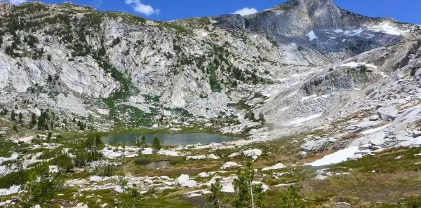 Ansel Adams wilderness in California's Sierra Nevada Mountains|An alpine lake in the Ansel Adams Wilderness of California||A Wildland Trekking guide prepares dinner on the trail||A hiker rests under a tree in the high Sierra|Backpacking group and guide pose before a trip|