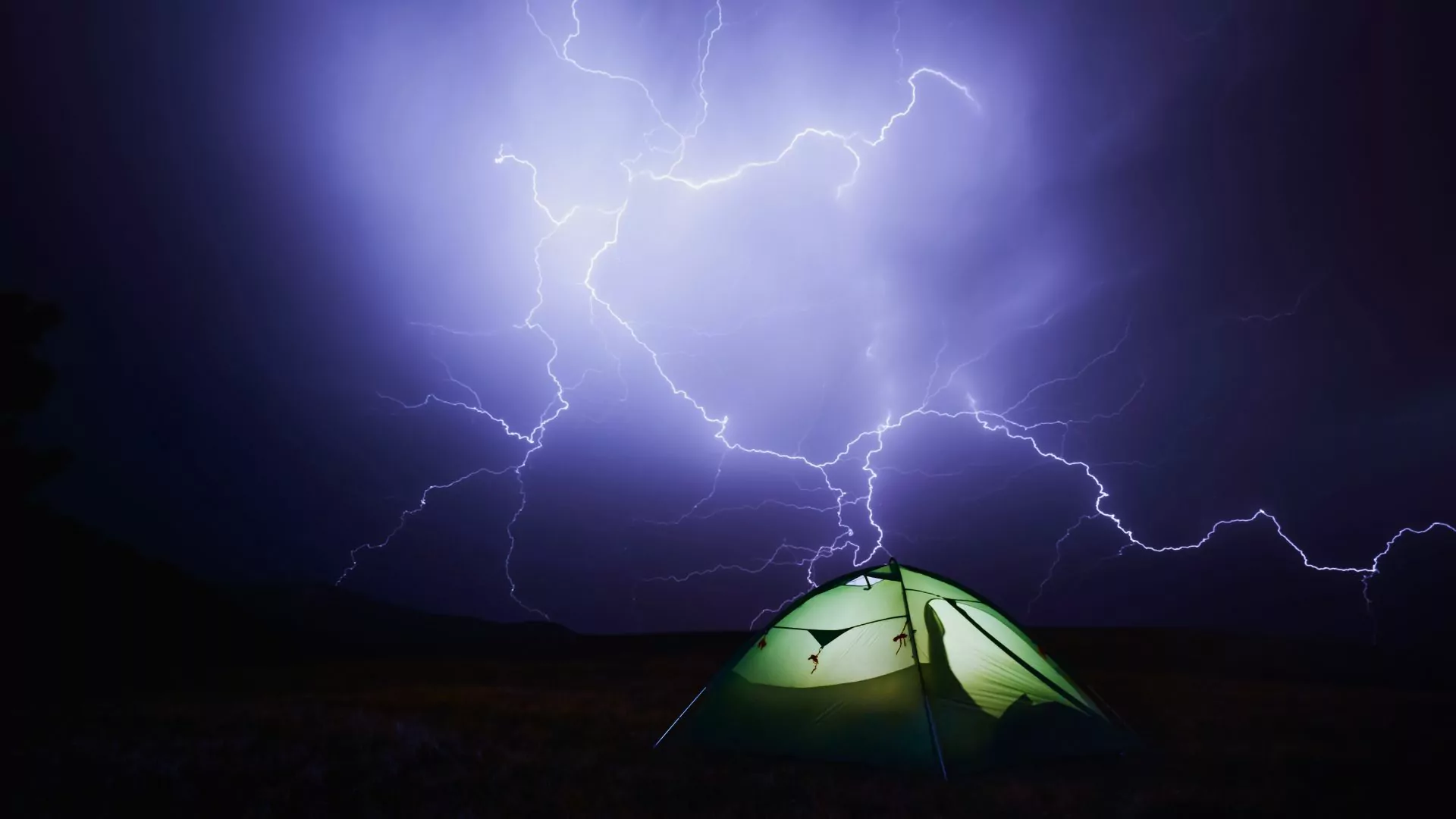 Lightning flashes in the night behind a tent