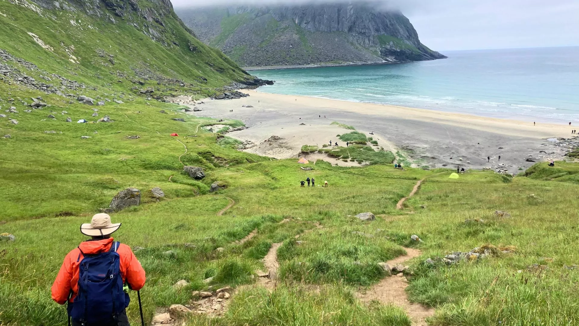 A person in a daypack hikes down a trail to the beach