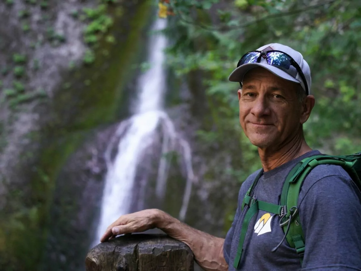 A man poses next to a waterfall