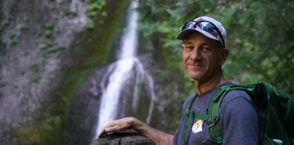A man poses next to a waterfall